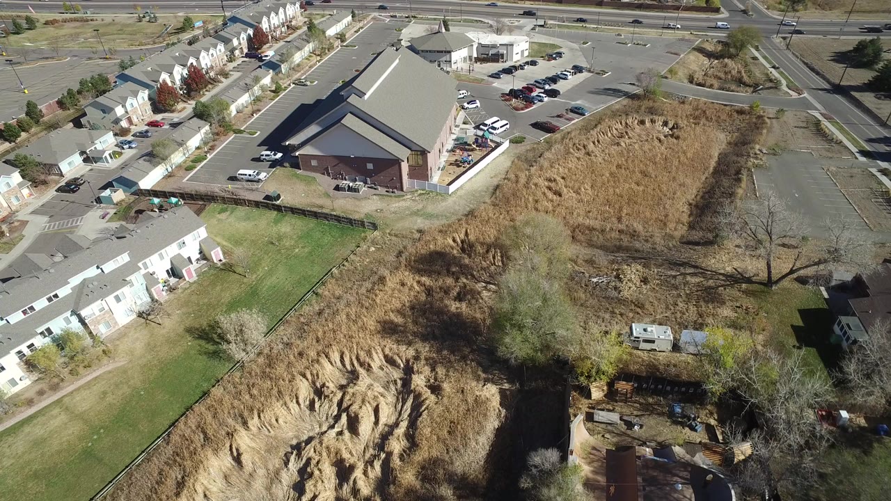 Aerial view of a construction area beside parking lots, roads, houses, grass, and trees.