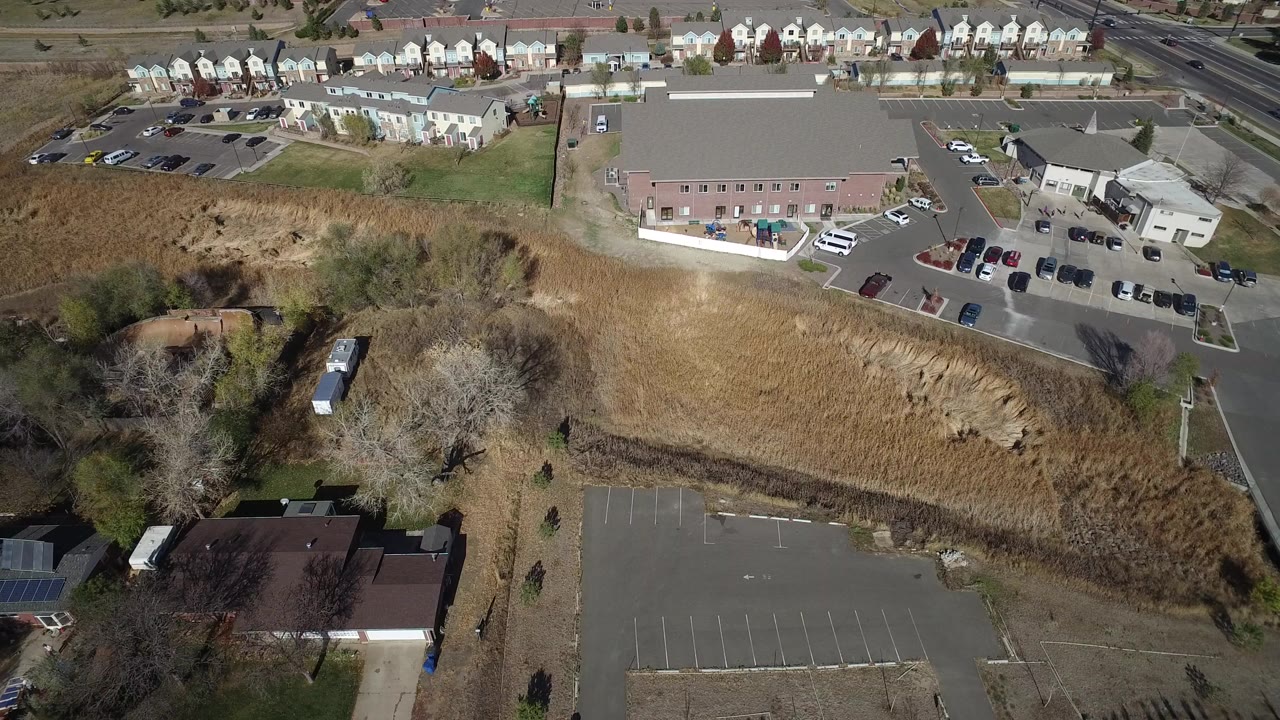 Aerial view of dry open ground, parking lots, houses, roads, and low buildings.