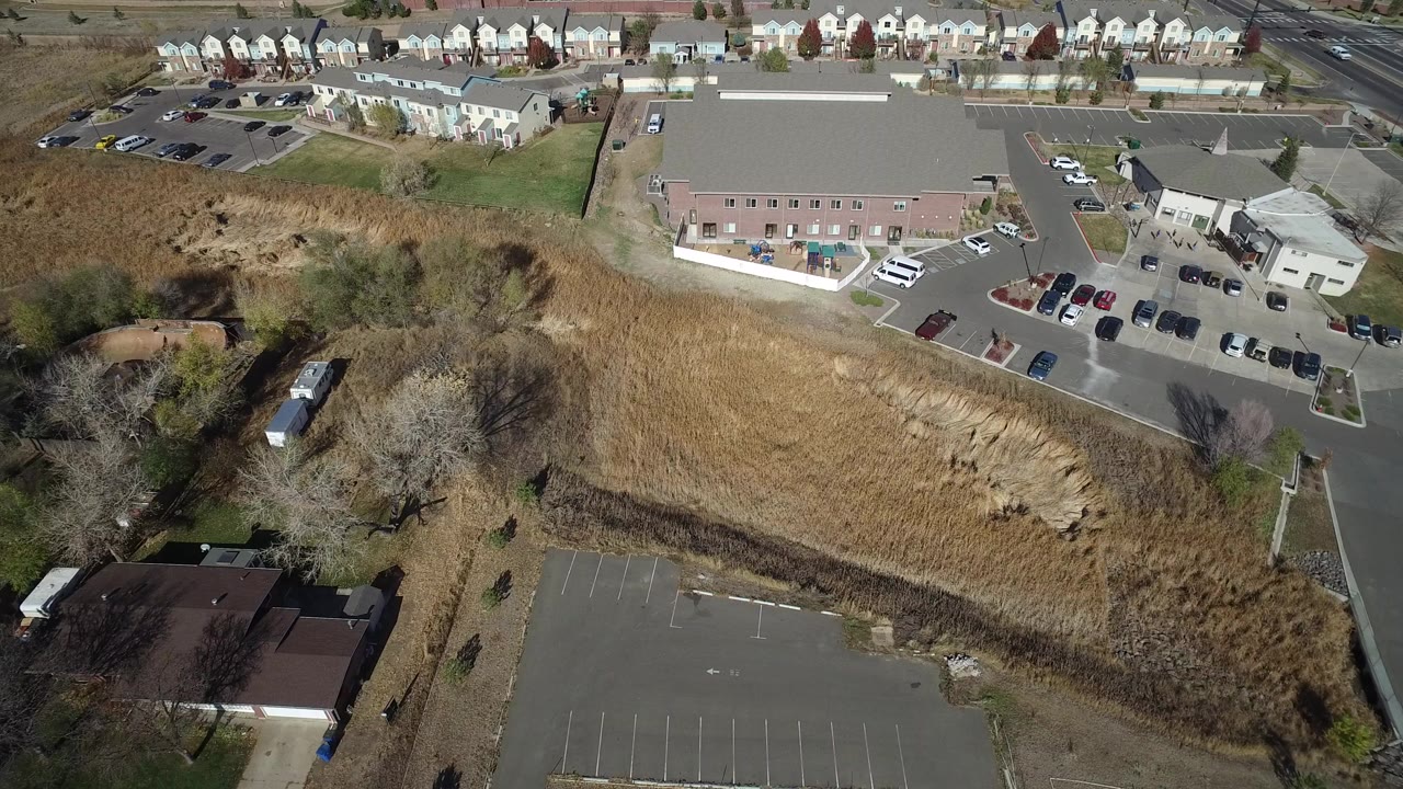 Aerial view of a parking lot, grassy drainage area, buildings, and homes.