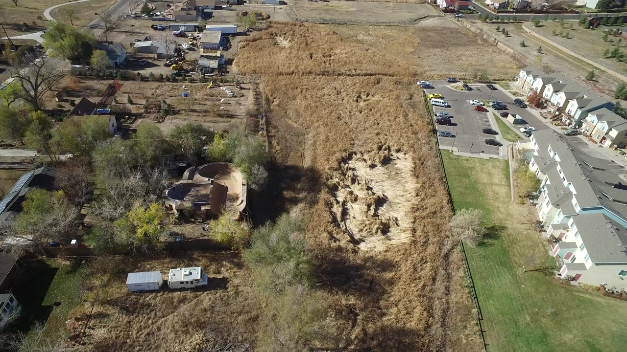 Aerial view of dry field, dirt pit, townhomes, road, and trees.