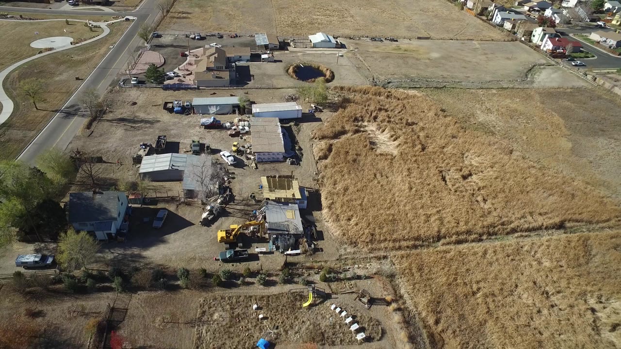 Drone view of a work yard next to dry grass and suburban homes.
