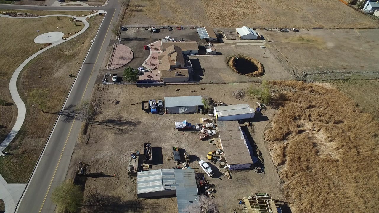 Aerial view of houses, road, sheds, dry lots, and a small pond.