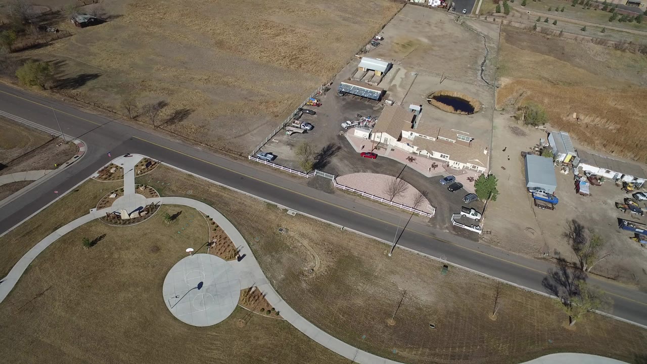 Aerial view of a road, curved park path, circular plaza, and small industrial yard.
