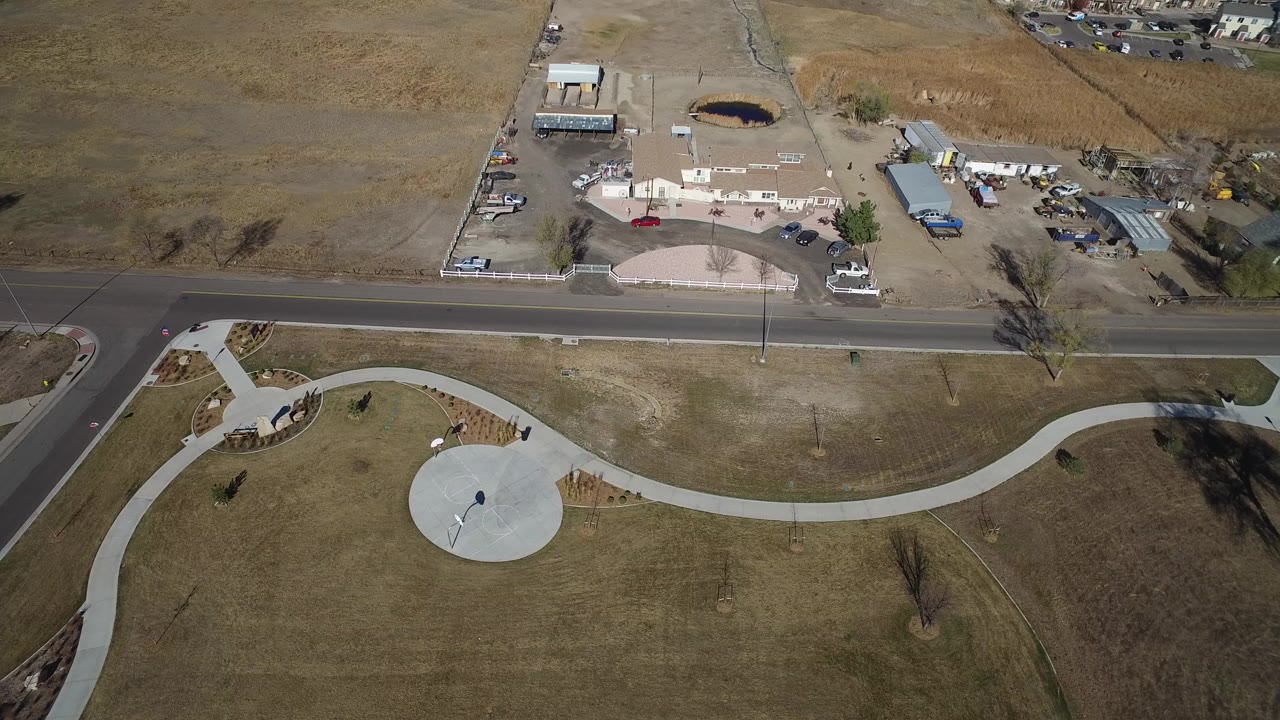 Overhead view of a roadside park path, open grass, low buildings, and parked cars.