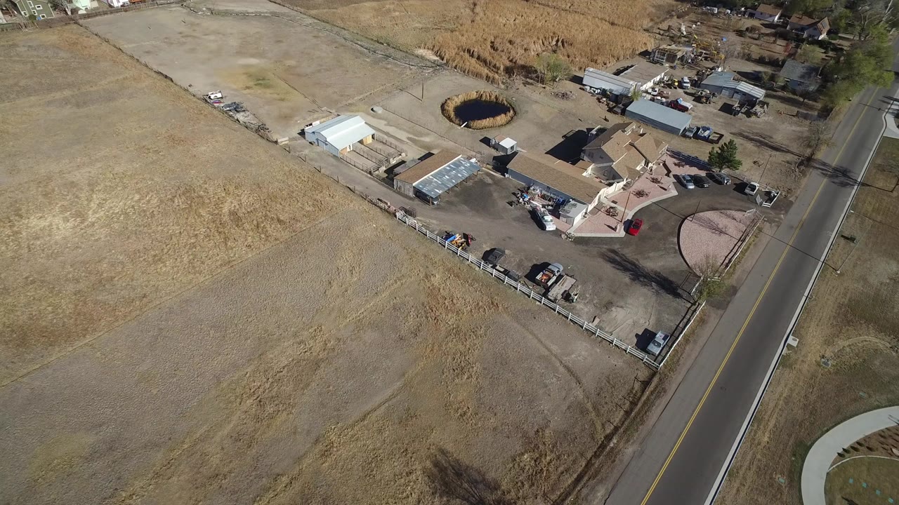 Aerial view of dry fields, a paved road, homes, and fenced lots.