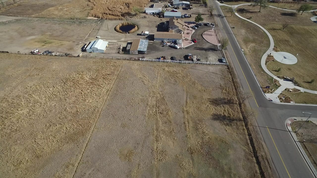 Aerial view of dry fields beside a paved road and developed property.