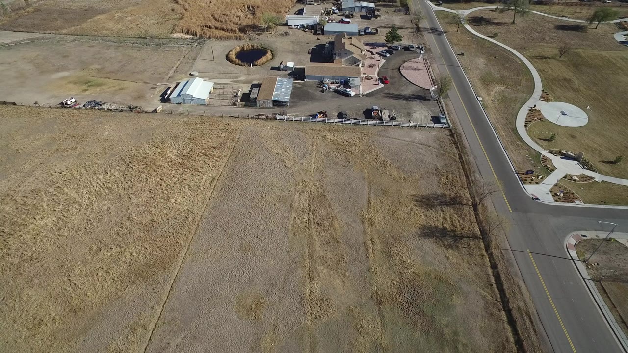Aerial view in Hidden Lake, Colorado with dry grass parcels filling the foreground, a straight road at right, curving sidewalks, and a developed property area near the top edge.