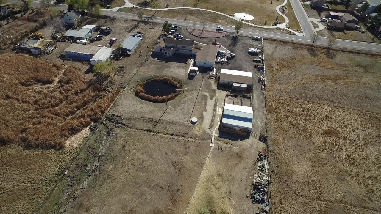 High aerial view of dry lots, a pond, small buildings, and a road.