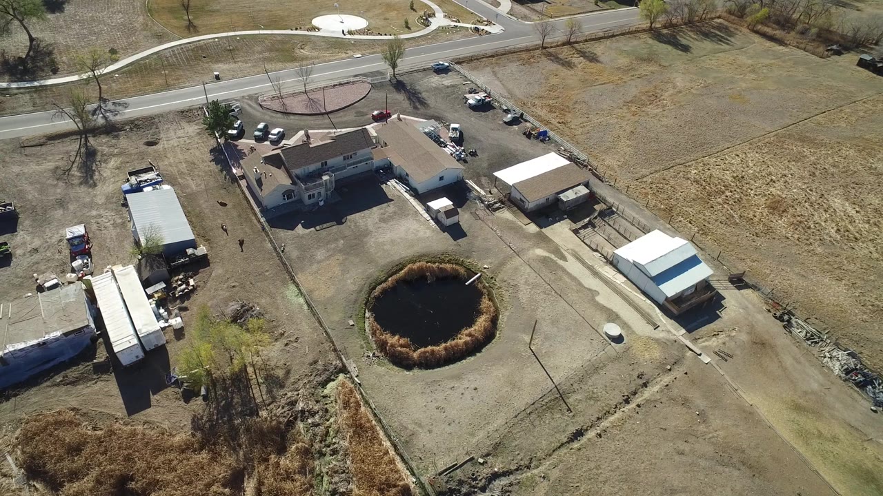 Oblique aerial of a rural building beside dry fields and a dark round yard feature.