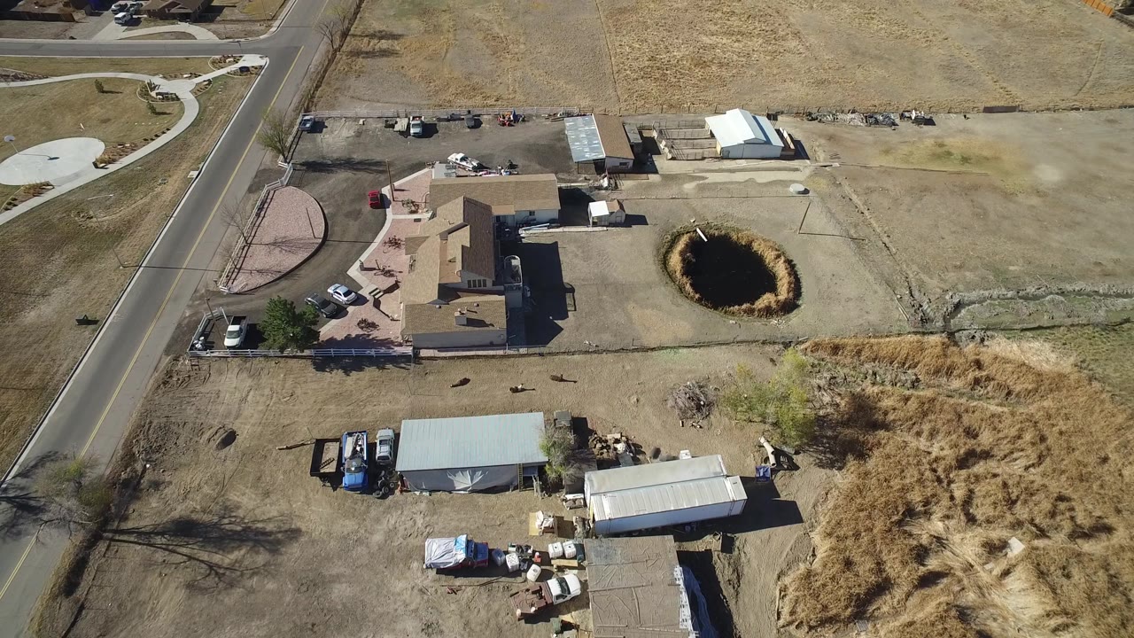 Aerial view of houses and a dark circular ground feature beside dry grass and open land.