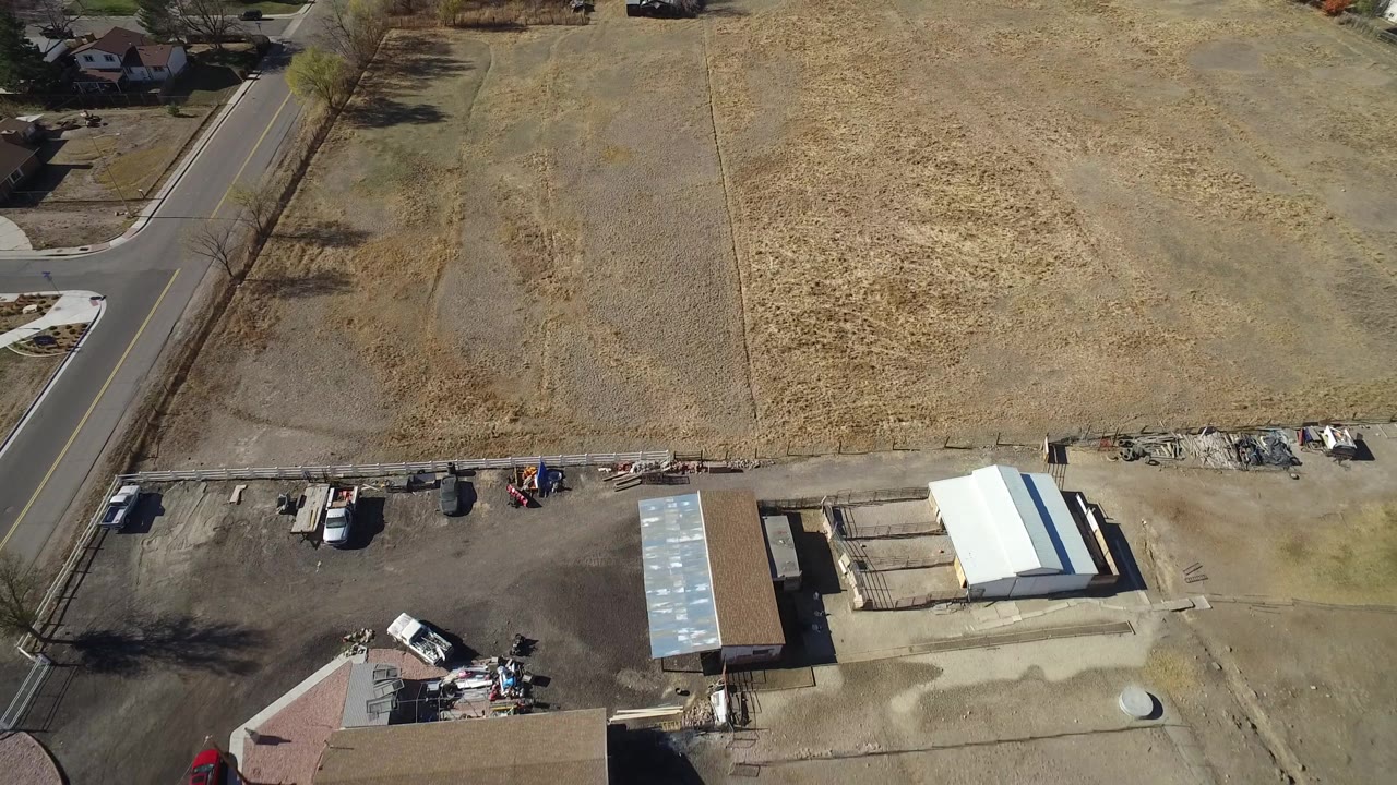 Aerial view in Hidden Lake, Colorado with the road along the left, dry acreage across the top, and construction materials and sheds below, with no visible people.