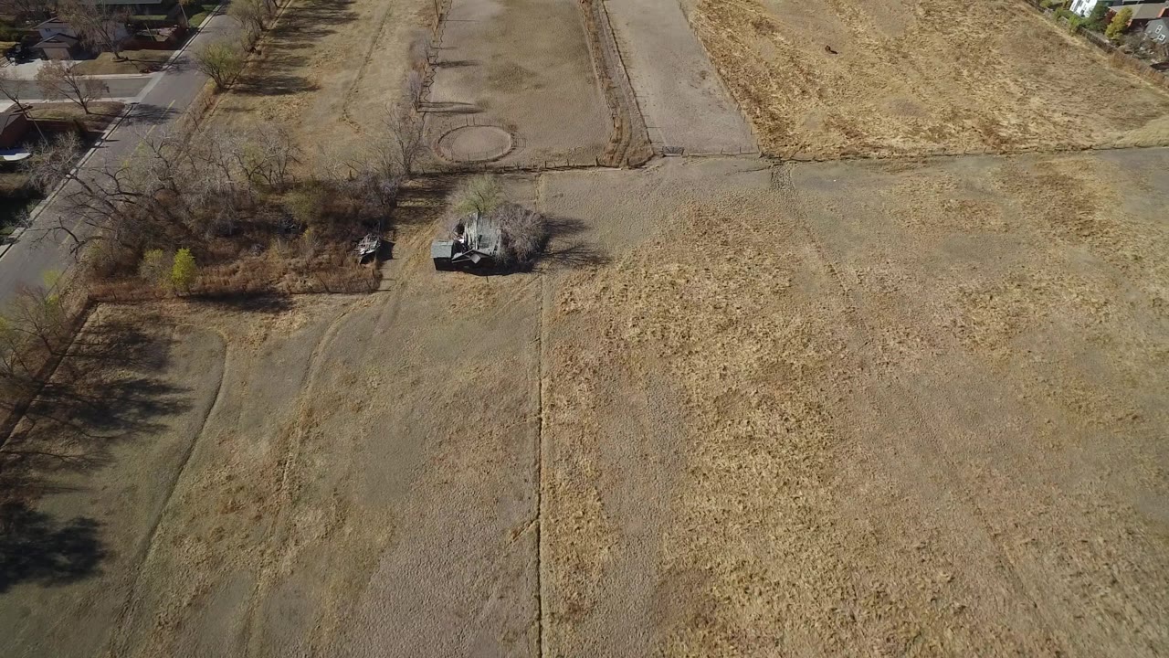 Overhead view of tan fields, road lines, trees, and nearby homes.