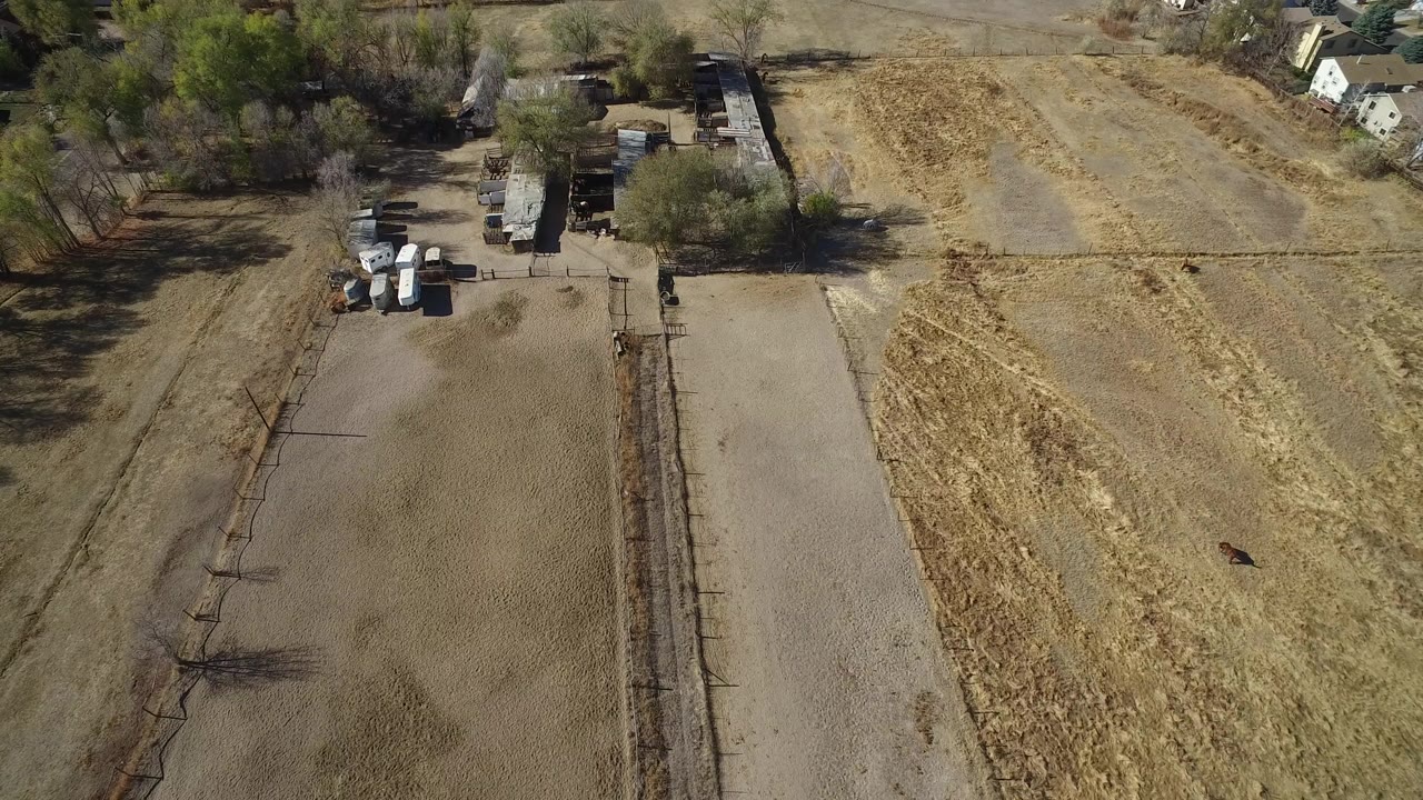 Overhead view of fenced dry lots beside trees and small structures.