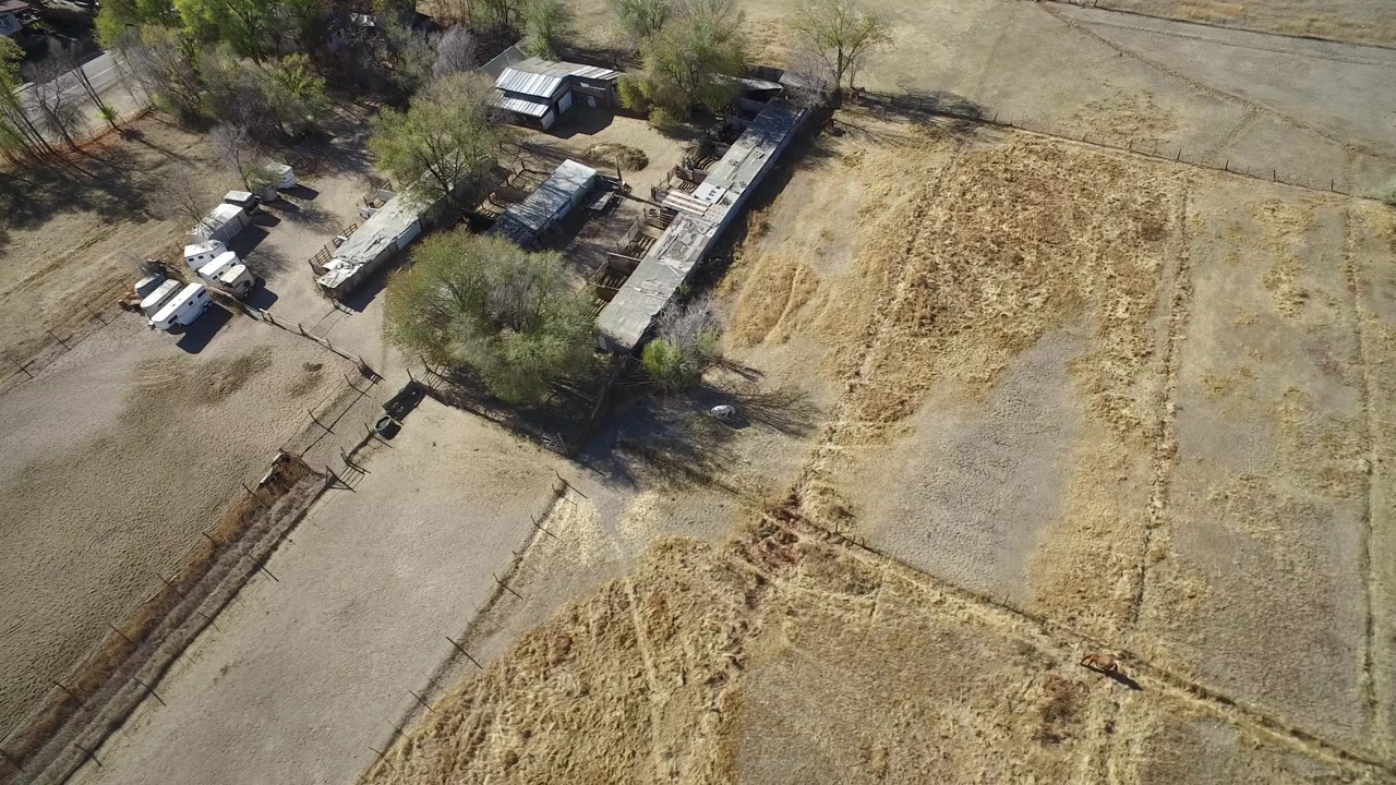 Overhead frame in Hidden Lake, Colorado with a pale rectangular lot, rough grass patches, trees, long low buildings or sheds, light-colored parked vehicles, and no visible people.