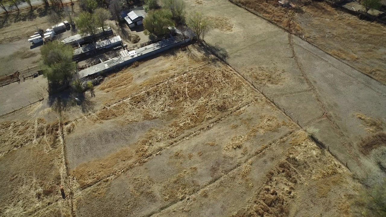 Overhead view of dry fields, roads, trees, and low buildings.