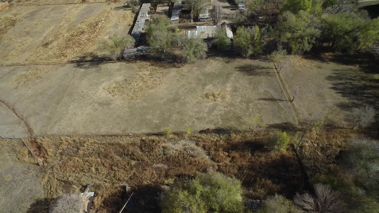 Aerial view over dry fields, brush, trees, and small rural buildings.