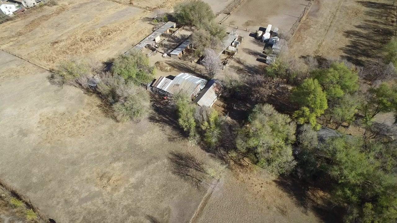 Overhead rural property with trees, dry fields, and small buildings.