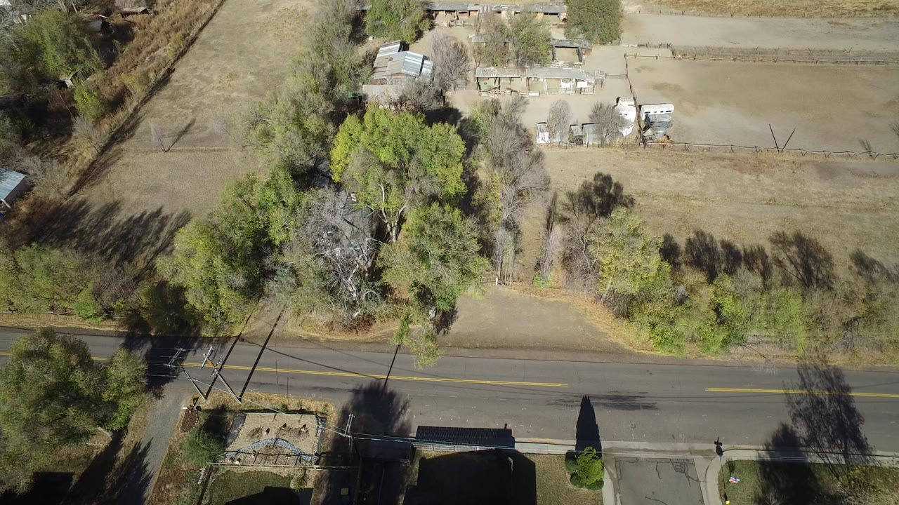 Overhead rural road beside trees and fenced farm lots.