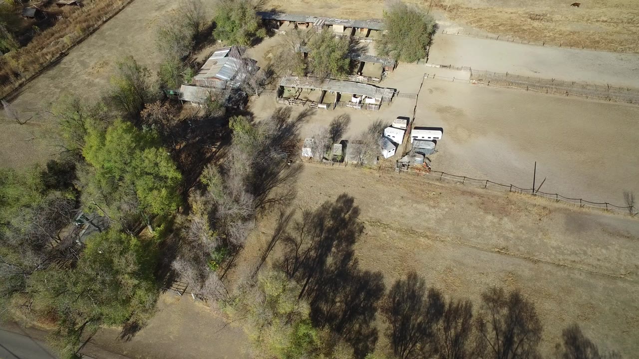 Overhead view of a rural property beside dry fields and trees.