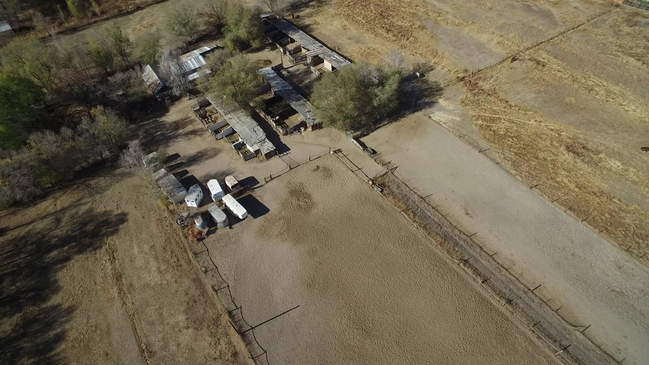 High aerial frame over Hidden Lake, Colorado showing dry open ground, a pale road, scattered trees, small buildings, parked vehicles or trailers, and no visible people.