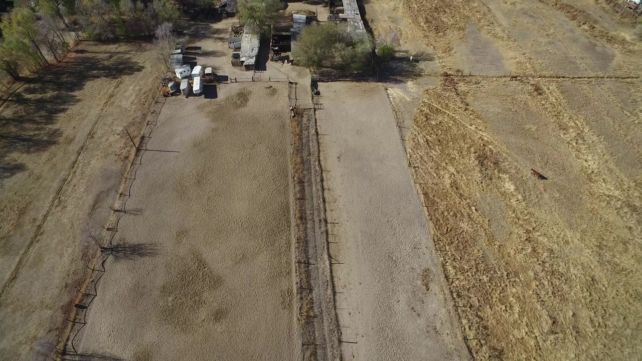 Overhead view of dry fields, a dirt road, fences, and small structures.