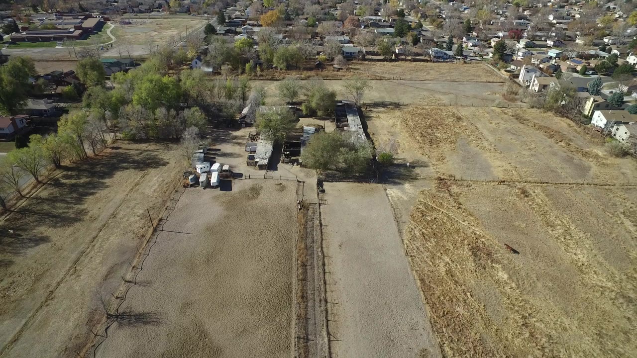 Aerial view over dry fields, trees, houses, and a residential area.