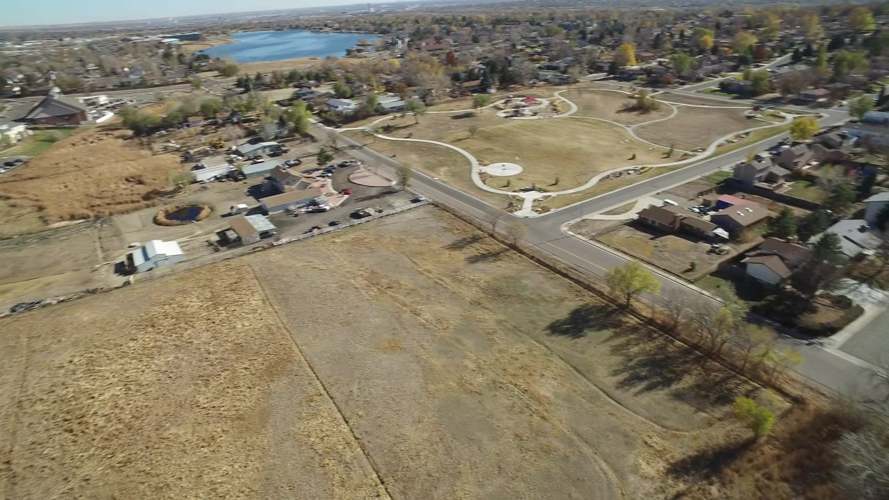 Aerial view over dry fields, roads, homes, parkland, and distant water.
