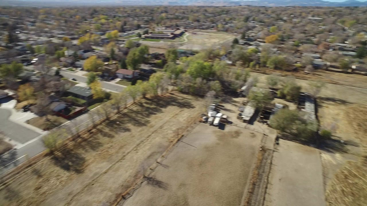 Aerial view over dry open land, trees, roads, and houses.