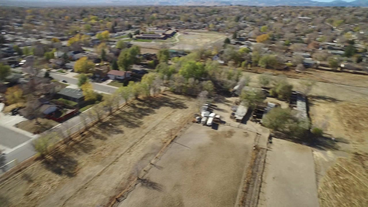 Aerial frame in Hidden Lake, Colorado with a bare rectangular plot below, a road at left, houses around the upper edge, and no visible people.