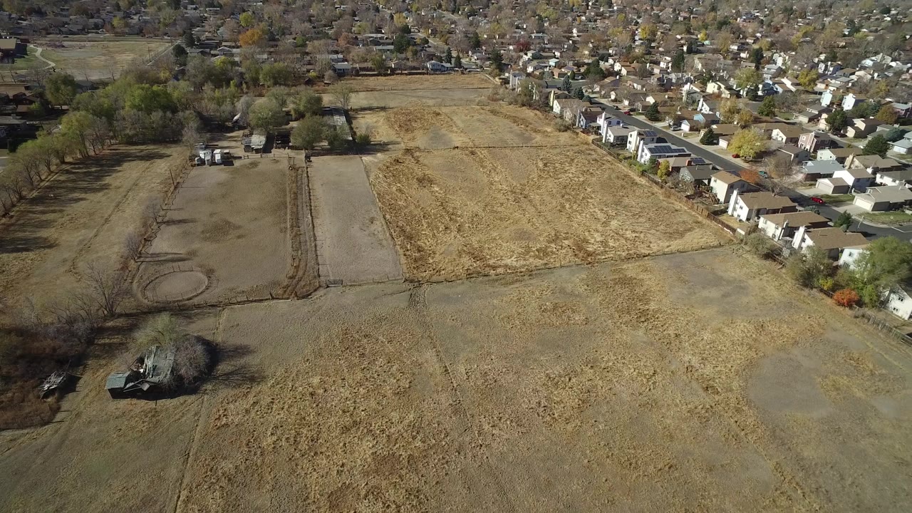 Aerial view in Hidden Lake, Colorado with tan open ground across the lower frame, a dirt track and bare plot to the left, houses to the right, and no visible people.