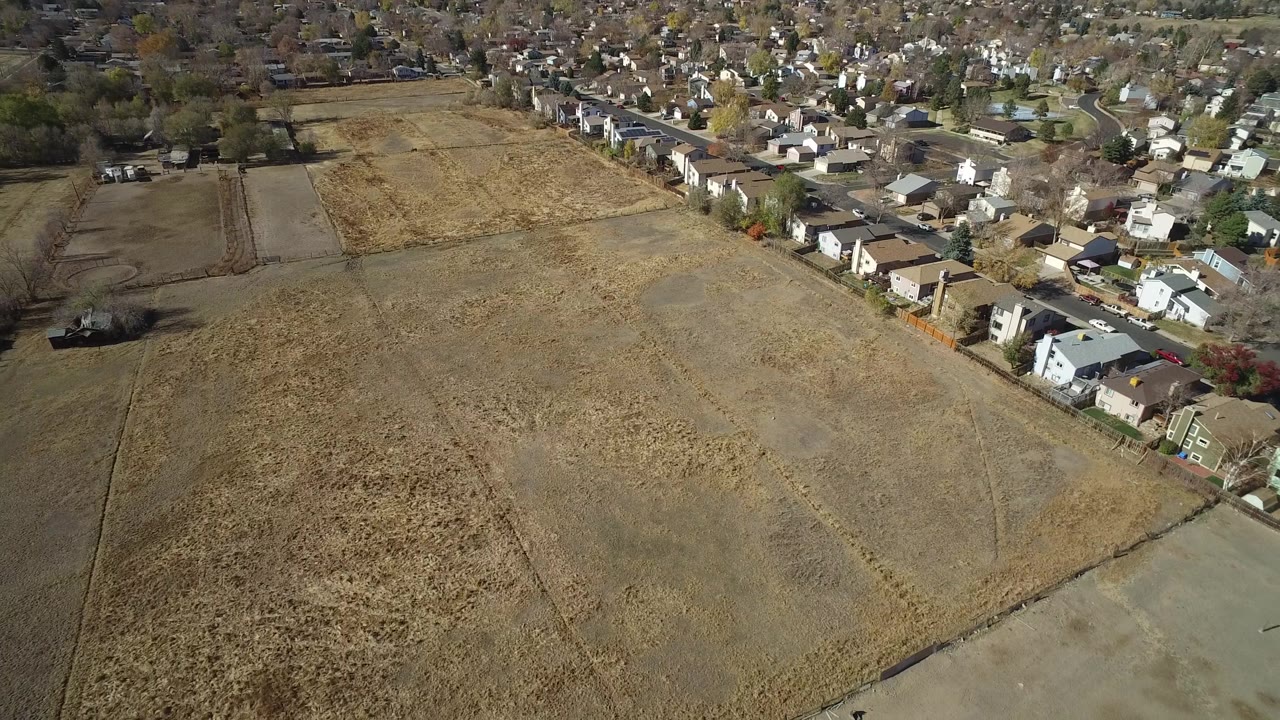 Elevated view in Hidden Lake, Colorado, with a large dry field across the center and dense housing along the upper edge, with no visible people.