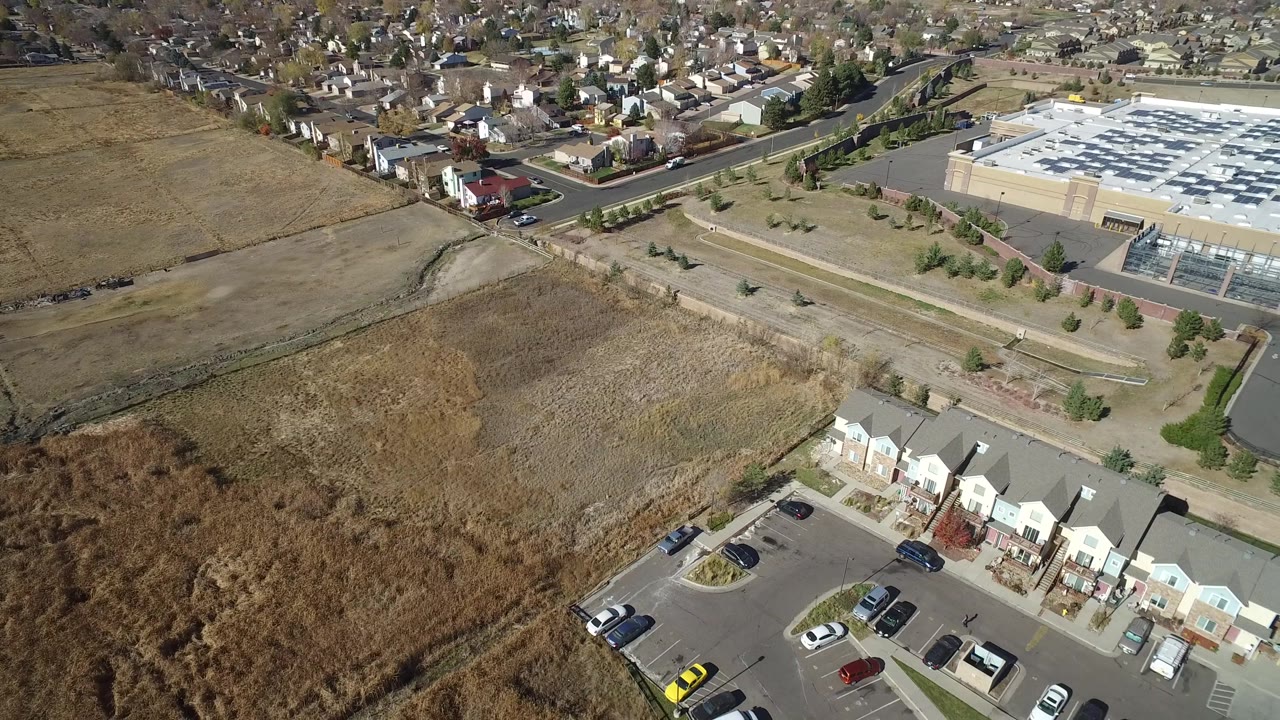 Hidden Lake, Colorado aerial view with the townhome row slightly lower in frame, dry fields and drainage marks across the center, the mall building in the background, and no visible people.