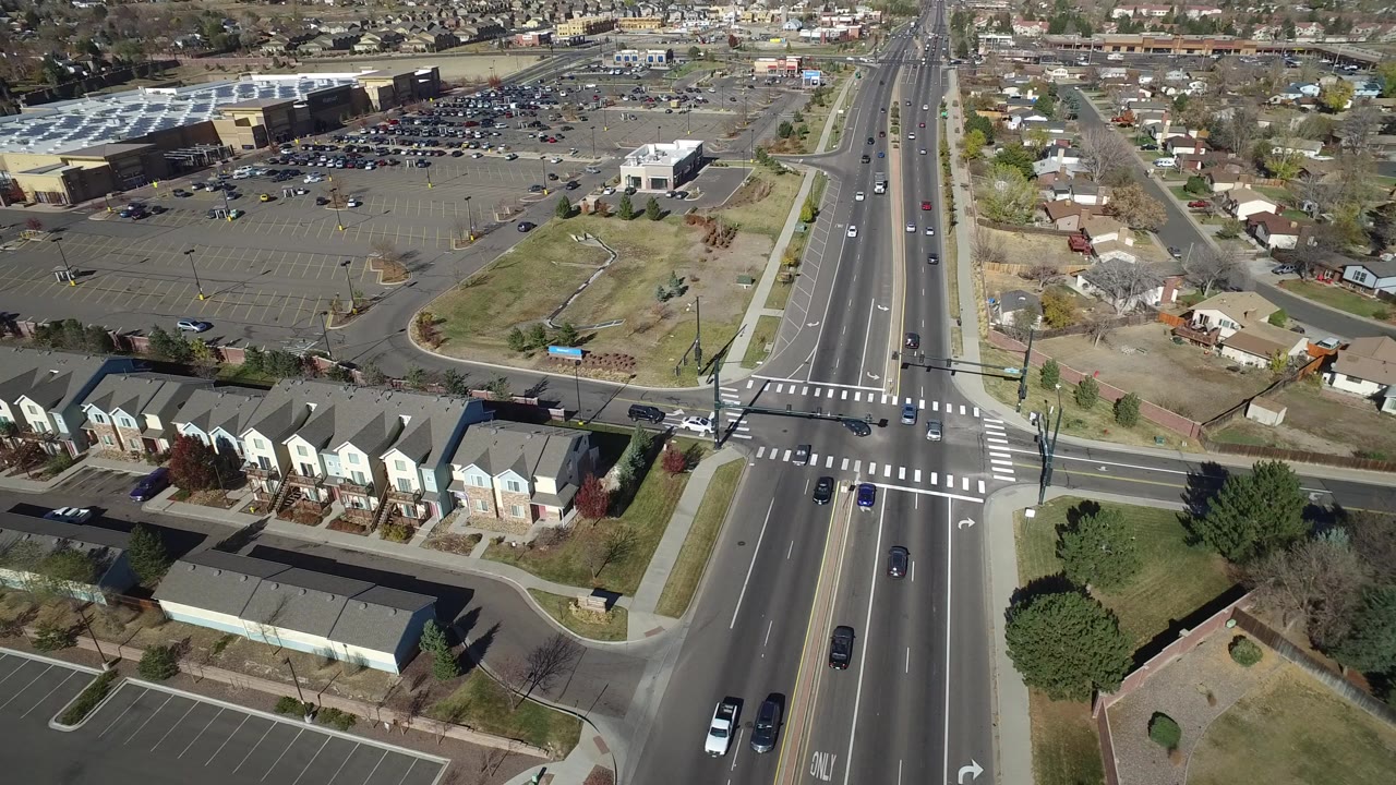 Overhead view of a wide suburban intersection beside homes and parking lots.
