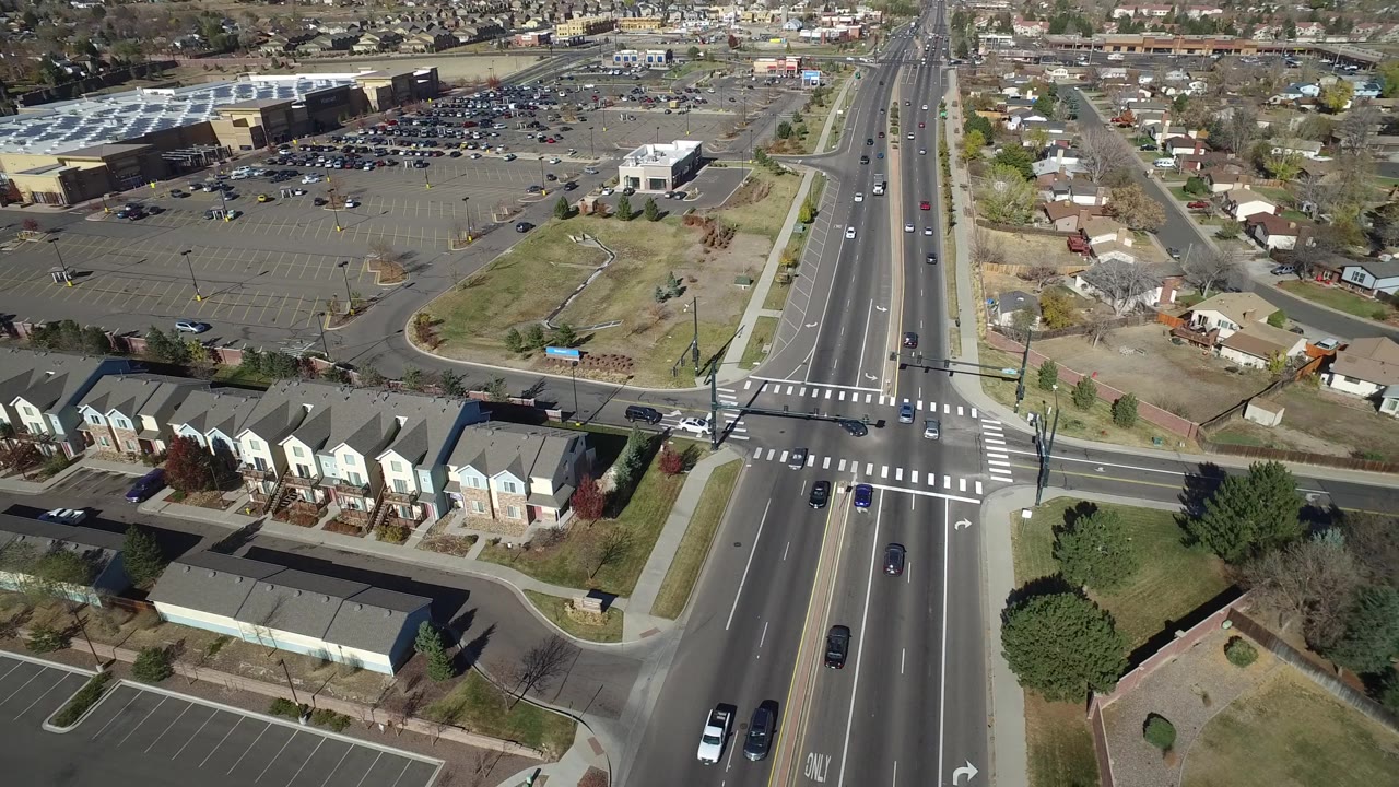 Aerial frame in Hidden Lake, Colorado with the main road running vertically past townhomes, side streets, parked cars, parking lots, and no visible people.