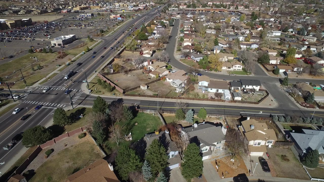 High aerial frame of Hidden Lake, Colorado showing a diagonal multi-lane road, foreground rooftops, side streets, parked cars, and no visible people.