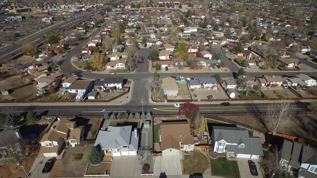 Aerial view of houses, yards, and a wide road through a residential neighborhood.
