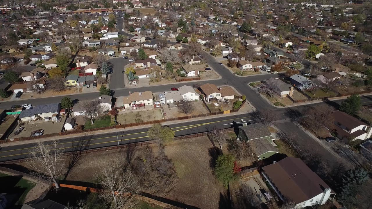 Overhead suburban neighborhood with homes, roads, and fenced lots.