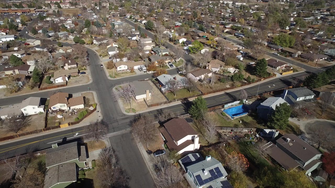 A high-angle aerial frame over Hidden Lake, Colorado shows single-family houses, intersecting streets, bare trees, parked vehicles, and no visible people.