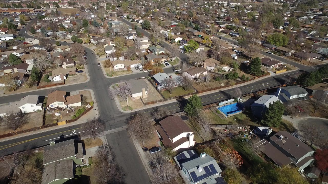 An elevated Hidden Lake, Colorado view centers on rooftops, a larger road, fenced yards, leafless trees, and a bright blue backyard pool, with no visible people.