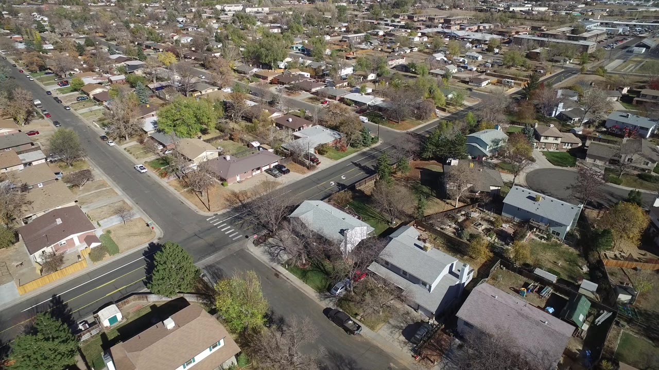 High aerial frame over Hidden Lake, Colorado homes, a four-way street intersection, parked cars, yards, and scattered trees, with no visible people.