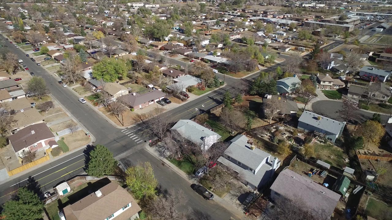 Overhead Hidden Lake, Colorado view with a painted crosswalk at a residential intersection, light-colored rooftops, fenced yards, parked vehicles, and no visible people.