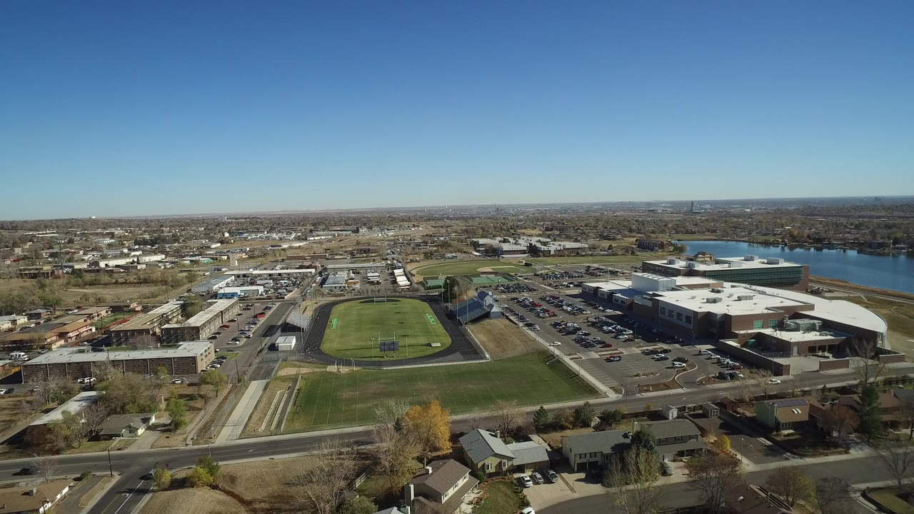 Aerial view of roads, a football field, parking lots, buildings, and a lake.