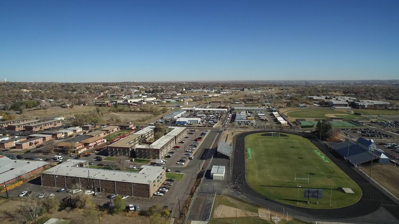 Opening aerial frame over a Westminster, Colorado sports field with track, bleachers, nearby parking lots, low buildings, and no visible people.