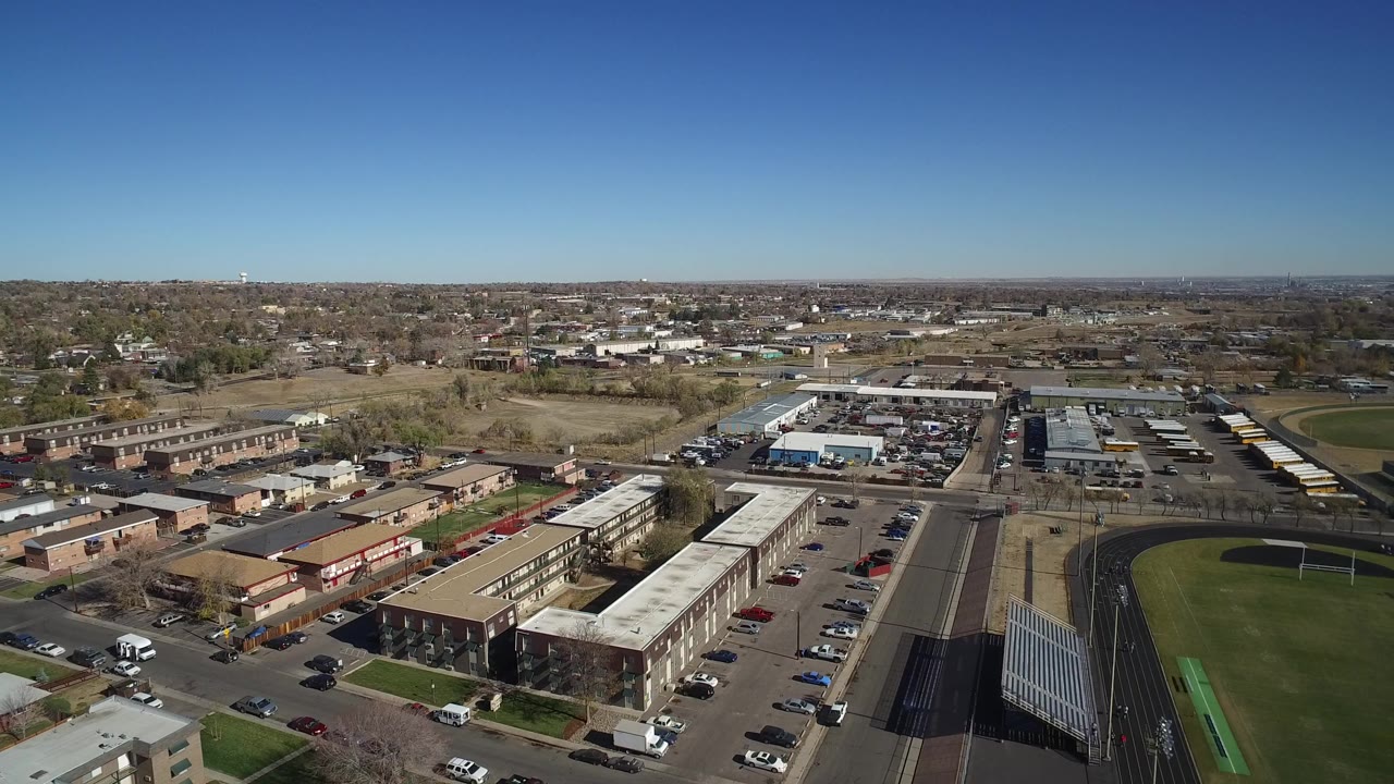 Aerial view over low-rise buildings, parking lots, streets, and a stadium track.