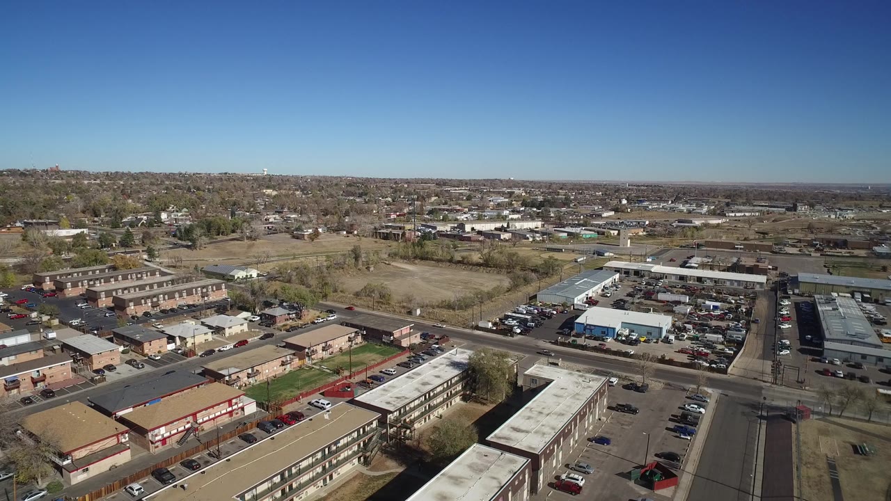 Aerial view in Westminster, Colorado looking across low-rise apartment blocks, car parks, intersecting streets, distant homes, and no visible people.
