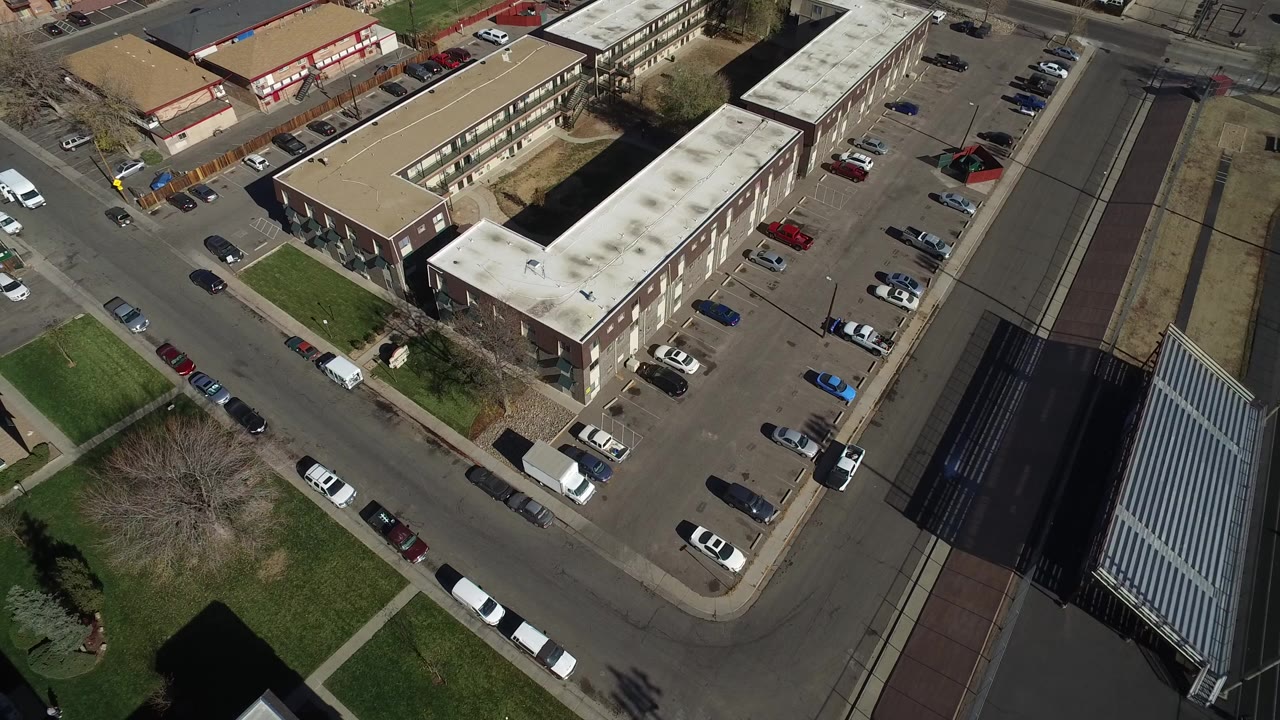 Overhead view of low-rise buildings, parking lots, roads, and grass.