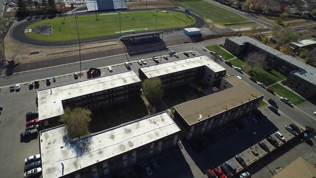 Aerial view of flat-roofed buildings beside a road and oval sports field.