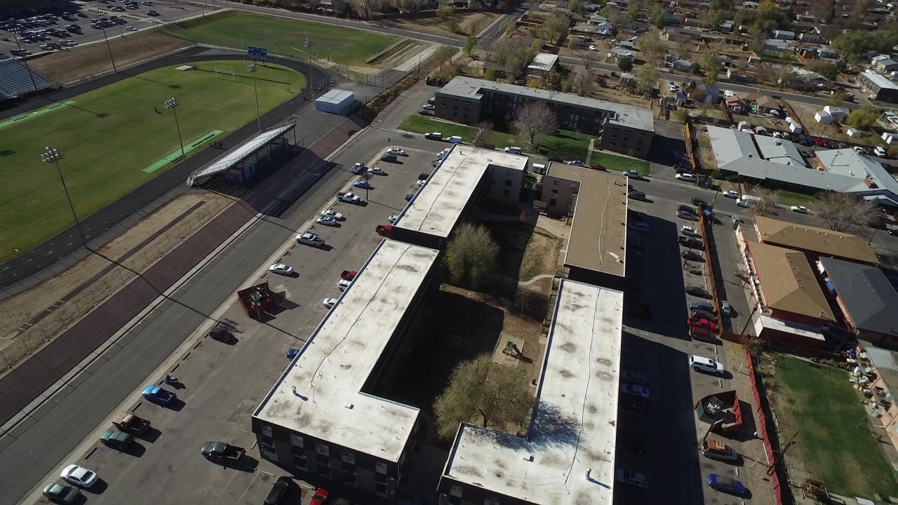 Aerial frame in Westminster, Colorado with the office roof and parking lot dominant, a road along the left side, sports fields beyond it, and no visible people.