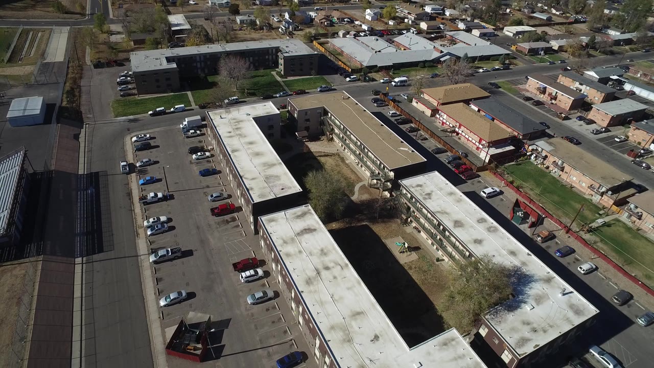 Aerial view over apartment buildings, parking lots, roads, and parked cars.
