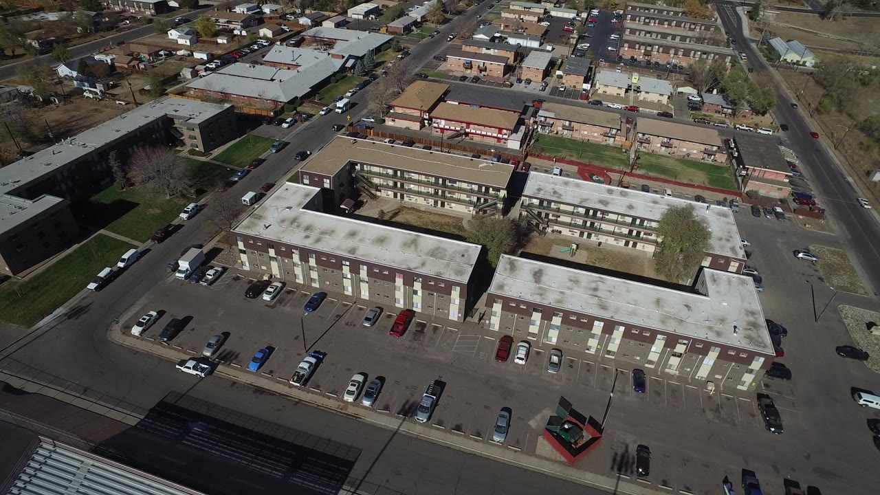 Opening aerial frame over Westminster, Colorado buildings with flat roofs, parked cars, surrounding roads, small lawns, and no visible people.